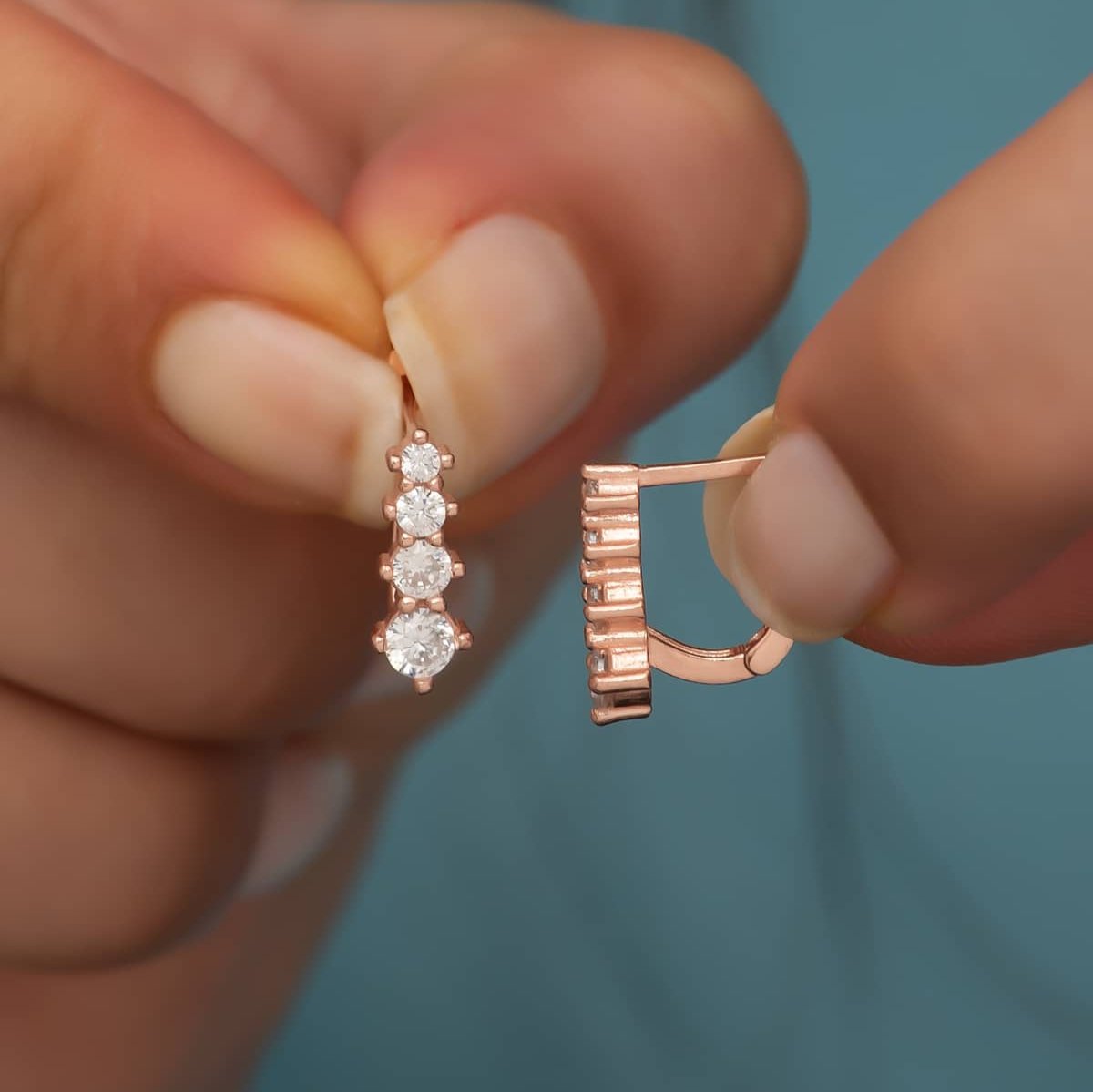 Rose-Goldene Ohrringe mit vier weißen Steinen gehalten von einer Dame